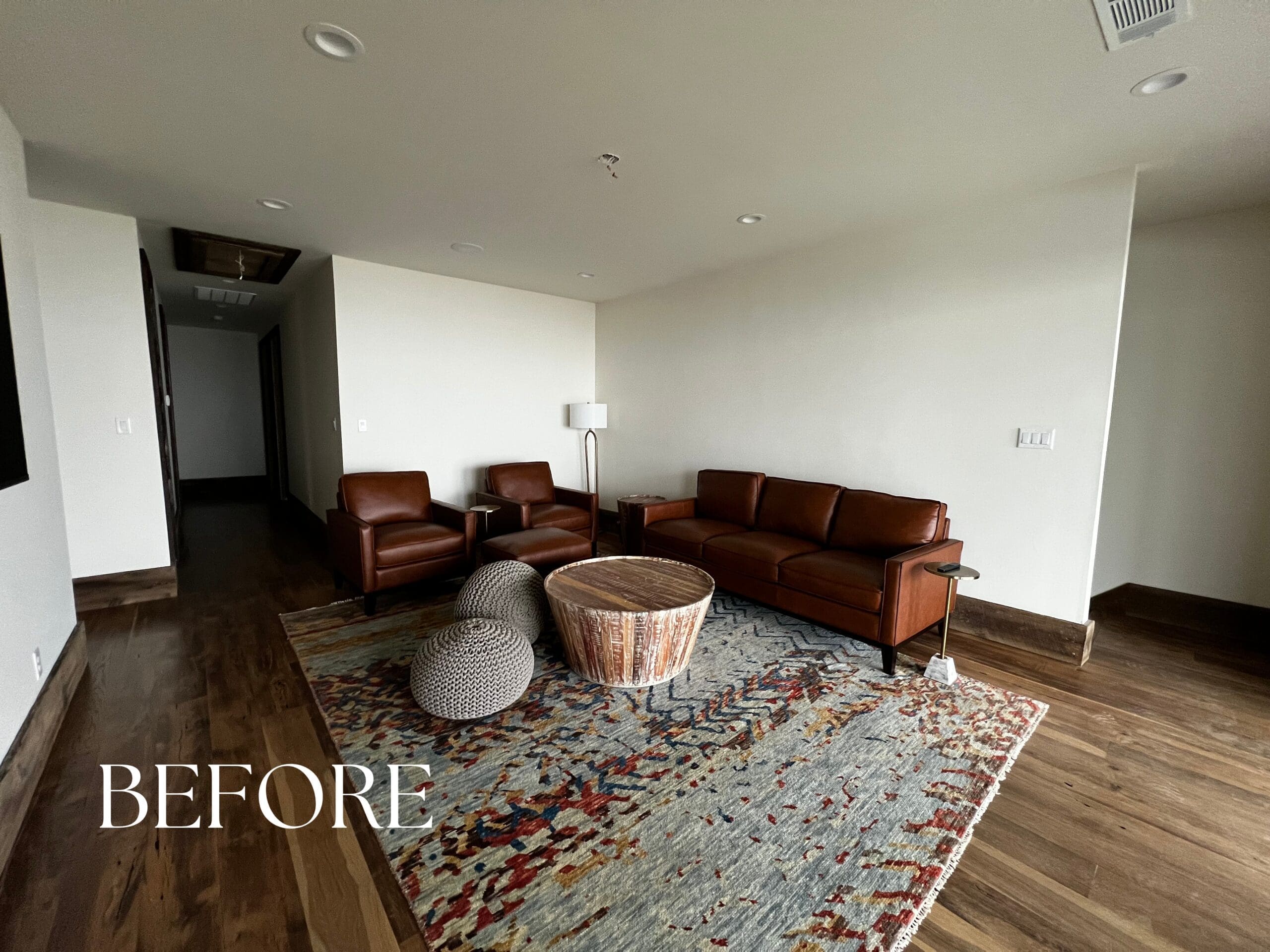 Before photo of an unstyled living room featuring bare white walls, a basic dark sofa, and large windows prior to a luxury interior design update.Before photo of an unstyled living room featuring bare white walls, a basic dark sofa, and large windows prior to a luxury interior design update.