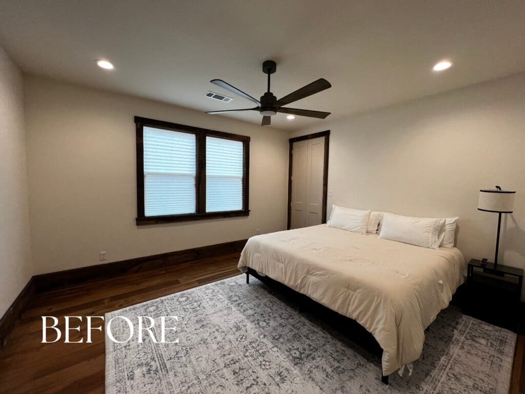 Before photo of an unfinished guest bedroom with bare white walls, dark hardwood floors, and minimal furniture prior to a luxury interior redesign.